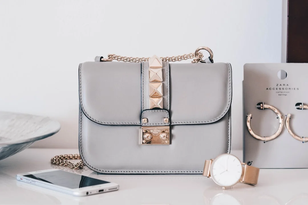A stylish woman in high-waist straight-leg jeans, a ribbed knit top, and white sneakers, carrying a minimalist leather crossbody bag against a sun-lit city backdrop